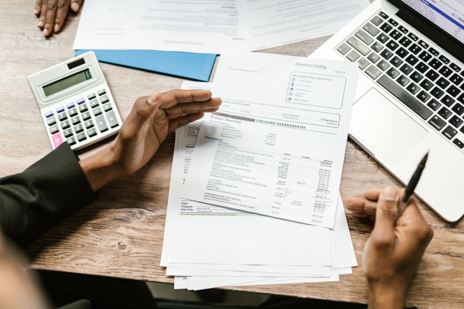Hands holding financial documents next to a calculator and laptop