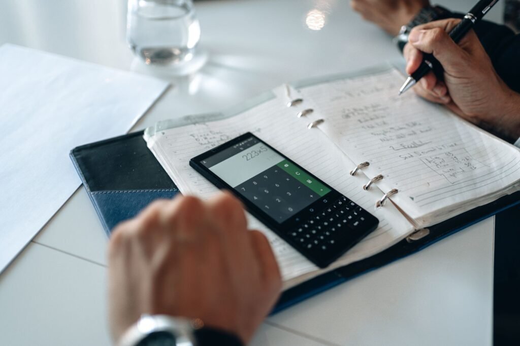 Close-up of hands writing in a notebook next to a smartphone calculator