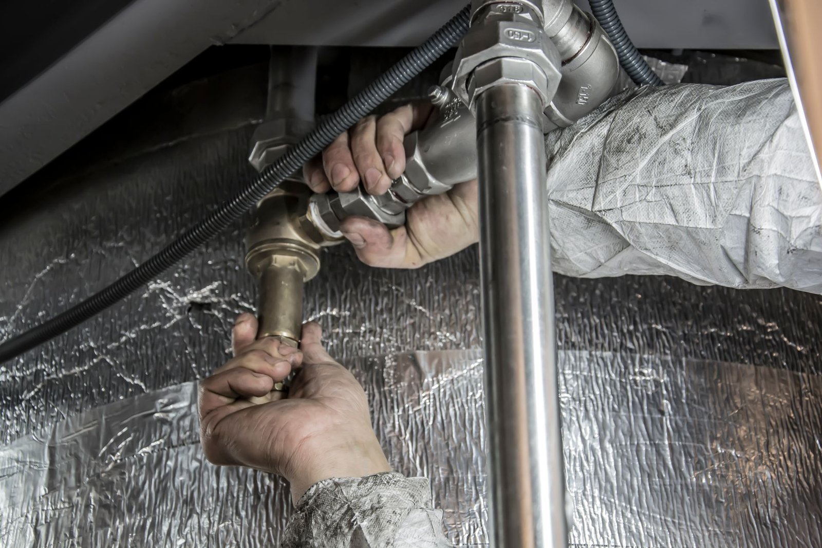 A plumber's gloved hands fitting steel pipes with a wrench