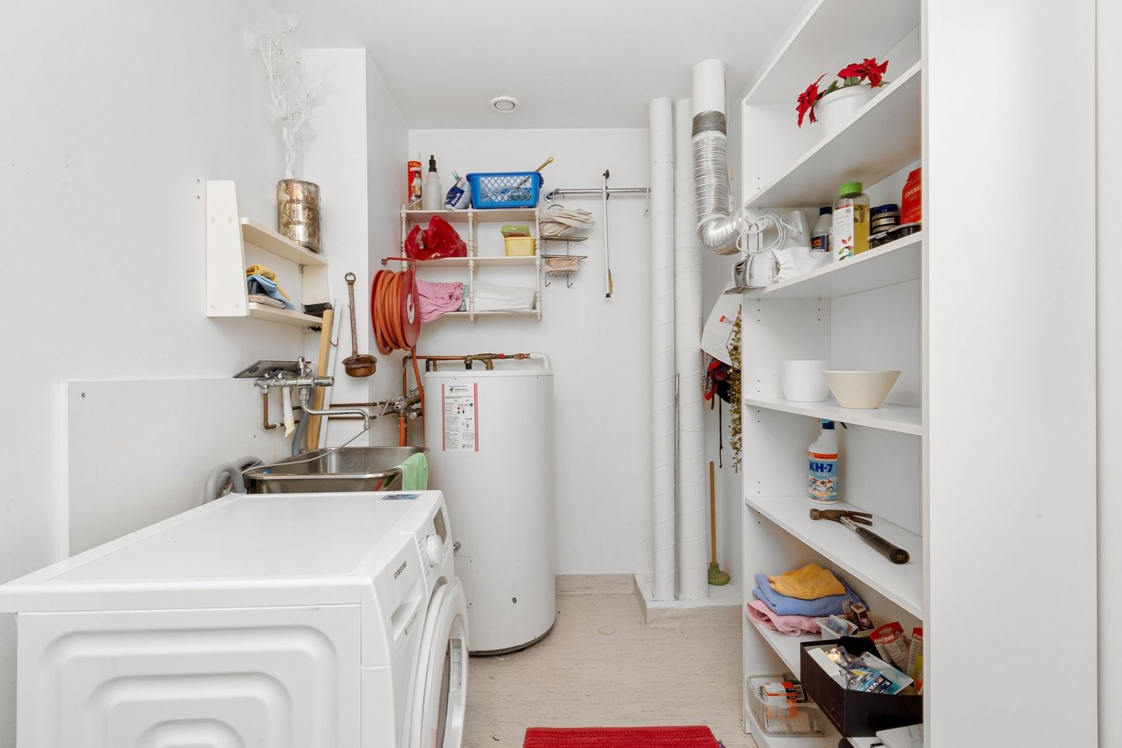 Home utility room with a washing machine, shelves, and a tank water heater